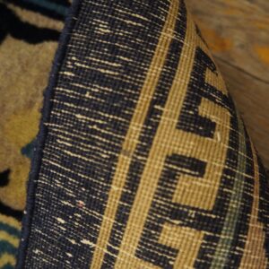 The edge of a rug is curled to reveal the navy and tan woven backing over rustic wood planks.