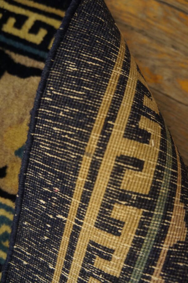 The edge of a rug is curled to reveal the navy and tan woven backing over rustic wood planks.