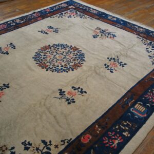 Low-pile cream rug with blue and pink floral motifs and a multi-layered brown and blue border on a wood floor.