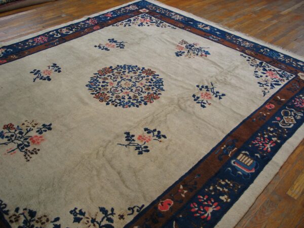 Low-pile cream rug with blue and pink floral motifs and a multi-layered brown and blue border on a wood floor.