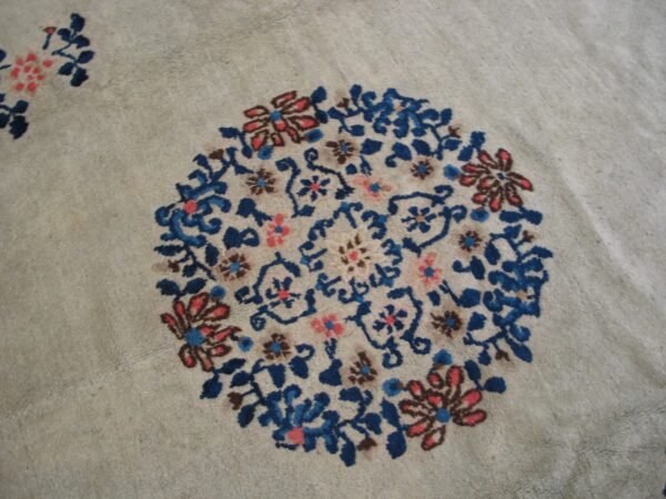 Close-up of a low-pile beige rug with an ornate blue and coral floral circular motif.