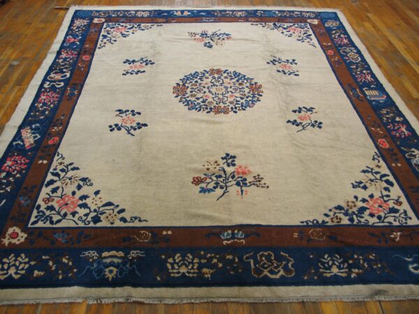 Cream floral rug featuring a blue medallion and intricate blue and brown multi-band borders on hardwood.