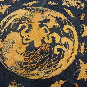 Low-pile dark blue rug featuring a central ochre dragon and scattered floral pattern.