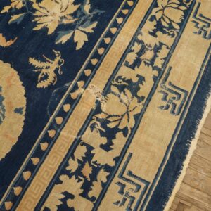Indigo rug with gold and light blue botanical and geometric patterns lies on worn wood floorboards.