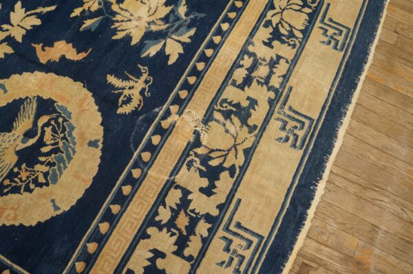 Indigo rug with gold and light blue botanical and geometric patterns lies on worn wood floorboards.