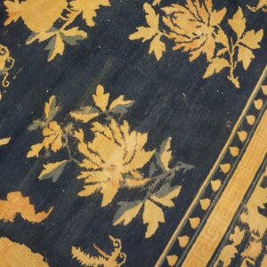 Low-pile rug detail showing golden floral designs, teal accents, and a wide striped yellow border on dark blue.