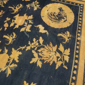 Worn, dark blue rug with faded yellow floral and butterfly motifs, featuring an ornate border.