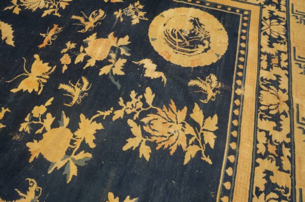 Worn, dark blue rug with faded yellow floral and butterfly motifs, featuring an ornate border.
