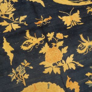 Detail of a dark blue rug with large stylized gold floral and insect designs and an ornate patterned border.