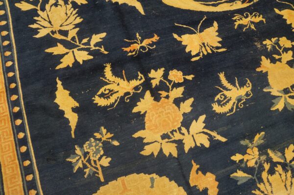 Detail of a dark blue rug with large stylized gold floral and insect designs and an ornate patterned border.
