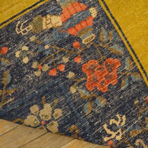 Navy blue rug with multicolored floral design and wide yellow border, curled slightly on wood planks.
