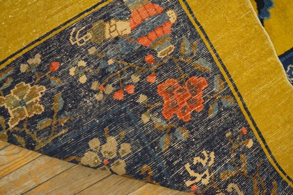 Navy blue rug with multicolored floral design and wide yellow border, curled slightly on wood planks.