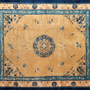Tan rug featuring a central medallion and scattered blue floral sprigs, surrounded by wide navy and teal borders.