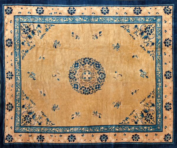 Tan rug featuring a central medallion and scattered blue floral sprigs, surrounded by wide navy and teal borders.
