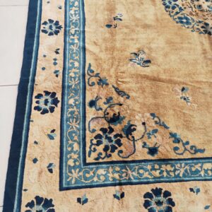 Faded gold rug featuring navy and teal floral motifs and an elaborate border lying on white tile.