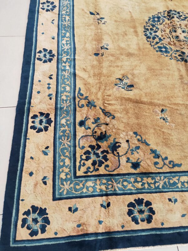 Faded gold rug featuring navy and teal floral motifs and an elaborate border lying on white tile.