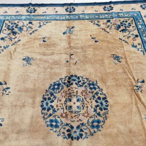 Ornate floral patterns in blue and teal cover a distressed tan rug lying on white tile flooring.