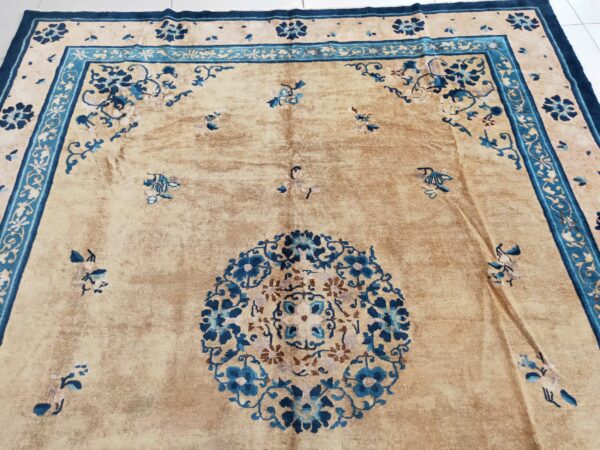 Ornate floral patterns in blue and teal cover a distressed tan rug lying on white tile flooring.