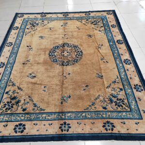 Tan area rug featuring detailed navy and teal floral borders rests on shiny white tiles.