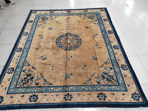 Tan area rug featuring detailed navy and teal floral borders rests on shiny white tiles.