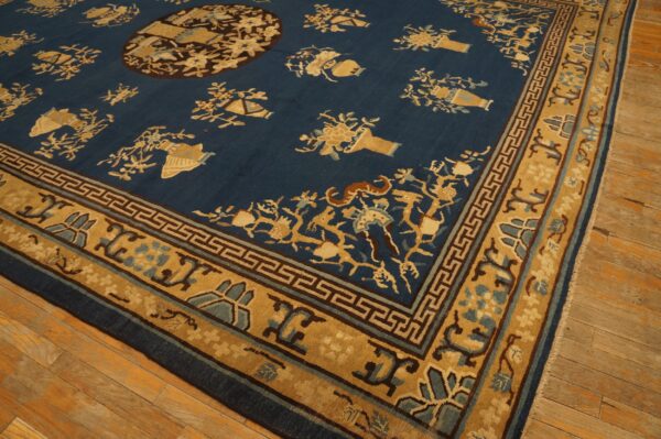 Low-pile dark blue rug with scattered tan floral motifs and a detailed border on rustic wood flooring.