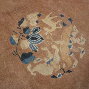 Muted tan rug detail showing a round pattern of blue foliage and light cream animal figures.