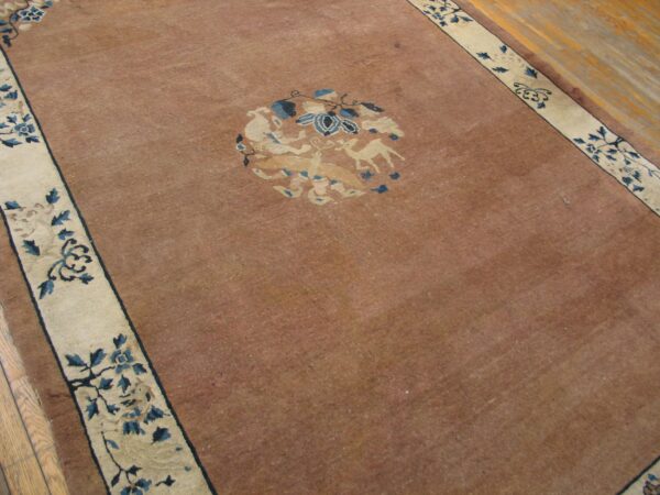 Low-pile russet rug with a central beige and blue animal motif bordered by dark floral vines on wood.
