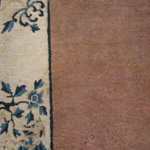 Dusty reddish-brown rug field next to a cream border patterned with dark and light blue florals.
