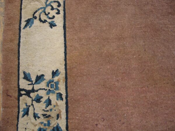 Dusty reddish-brown rug field next to a cream border patterned with dark and light blue florals.