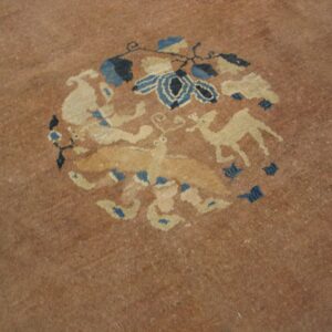 Rose-tan rug detail showing a round motif of light beige animal figures and stylized blue floral elements.