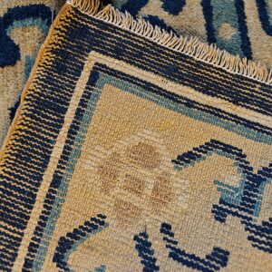 Tan and blue patterned high-pile rug detail next to its flatwoven backing with exposed fringe.