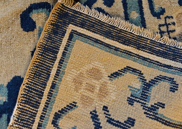 Tan and blue patterned high-pile rug detail next to its flatwoven backing with exposed fringe.