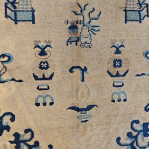 Close-up of low-pile beige rug featuring abstract dark blue and teal vase and scroll motifs.