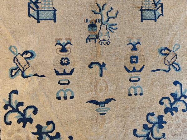 Close-up of low-pile beige rug featuring abstract dark blue and teal vase and scroll motifs.
