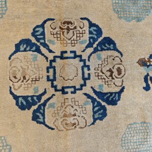 Low-pile beige rug featuring a detailed central geometric floral motif in indigo, light blue, and brown.