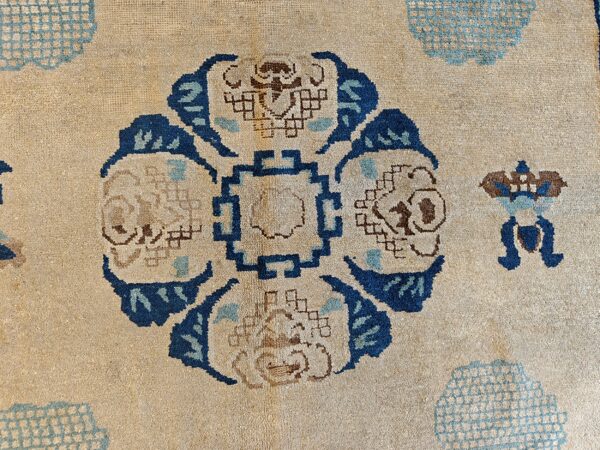 Low-pile beige rug featuring a detailed central geometric floral motif in indigo, light blue, and brown.