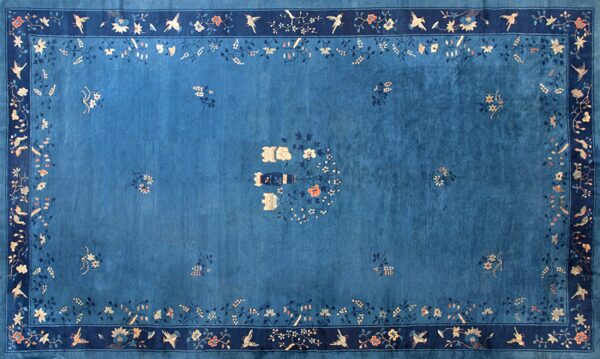 Saturated blue rug with a navy border, featuring delicate light blue and peach bird and floral patterns.