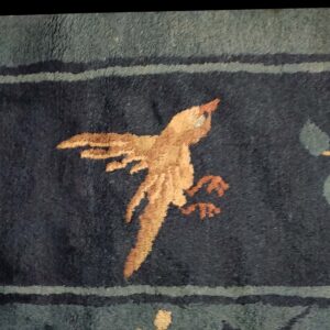 Dark blue, high-pile rug detail showing a tan bird motif, gray-green leaves, and a striped border.