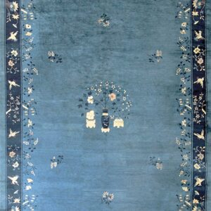 Teal rug featuring a central vase and scattered flowers, framed by a dark blue border with birds and vines.