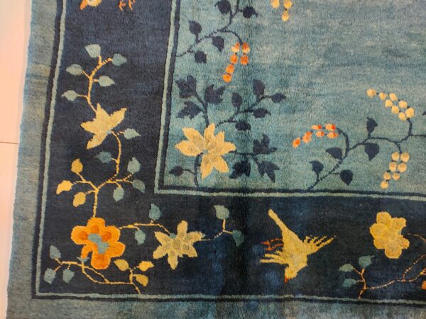 Teal rug field and navy border with stylized yellow, gold, and orange floral and bird motifs.