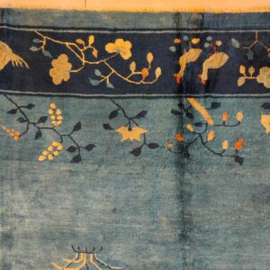 Teal blue rug with a dark border showcasing yellow flowers, vines, and stylized birds.