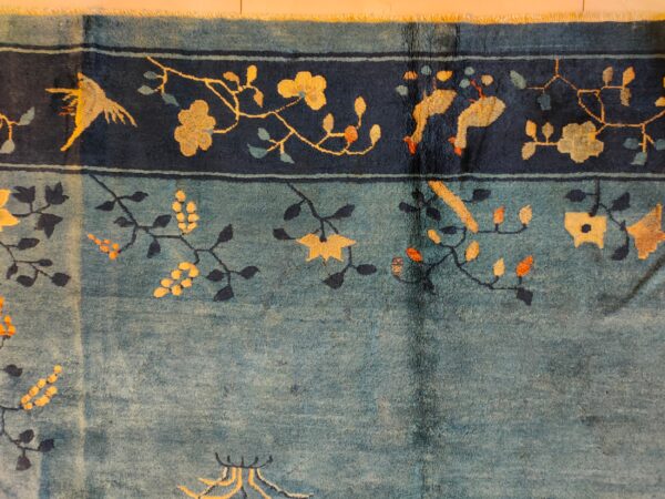 Teal blue rug with a dark border showcasing yellow flowers, vines, and stylized birds.