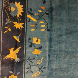 The teal rug field contrasts with the navy border decorated with yellow birds and blooming flowers.