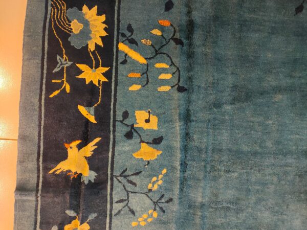 The teal rug field contrasts with the navy border decorated with yellow birds and blooming flowers.