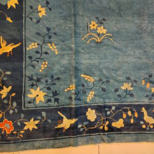 Blue rug with a dark blue border displaying yellow floral and bird patterns on light tile.