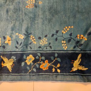 Blue-green medium pile rug displaying yellow floral vines and a dark navy border with gold birds.