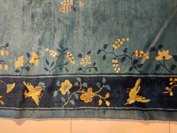 Blue-green medium pile rug displaying yellow floral vines and a dark navy border with gold birds.