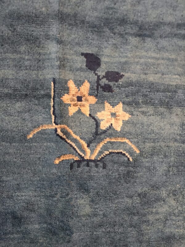 Detail of a medium pile blue rug with a beige and navy floral motif.