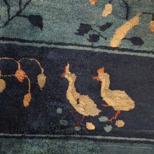 Detailed view of a medium-pile rug showing two beige birds in a navy border below a teal field.