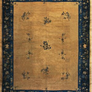 A golden rug with scattered blue floral sprigs and a wide dark blue border featuring winding flowers.
